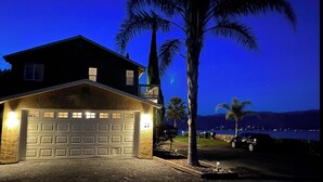 A two-story house with a garage, a balcony, and a view of a body of water at dusk.
