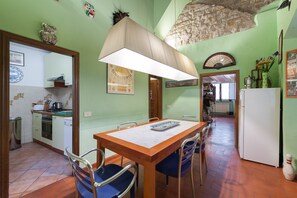 A dining area with a wooden table and chairs, a large hanging lamp, and a kitchen in the background.