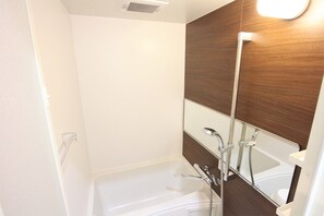 A modern bathroom with a white bathtub, a wooden vanity, and a large mirror.