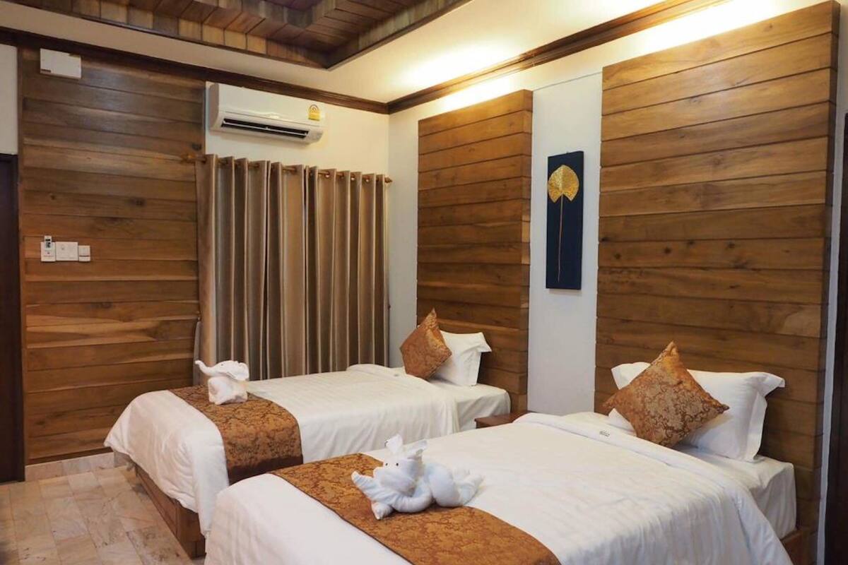 Une chambre d’hôtel avec deux lits, un lambris en bois, un climatiseur fixé au mur et un élément décoratif mural.