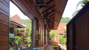 A covered outdoor area with wooden walls and a tiled floor, featuring a bar area with stools and a view of a house with a red roof. - Khum Sai Ngam Hotel & Resort (Songkhla)