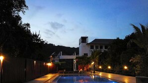 A swimming pool with tiled flooring, surrounded by a wooden fence and palm trees, with a building in the background. - Khum Sai Ngam Hotel & Resort (Songkhla)