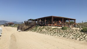 A desert resort with a wooden building, outdoor seating, and a sandy path leading to it.