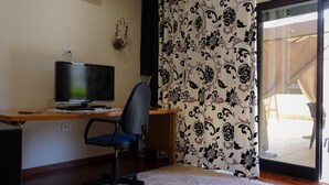 Una habitació amb escriptori, cadira, televisió i cortina amb un disseny.