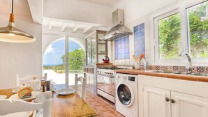 A kitchen with a washing machine, a stove, and a window overlooking greenery.