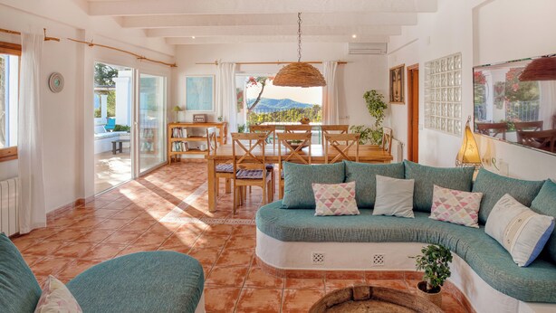 A spacious living area with a curved sofa, a dining table, and a view of a mountain through large windows.
