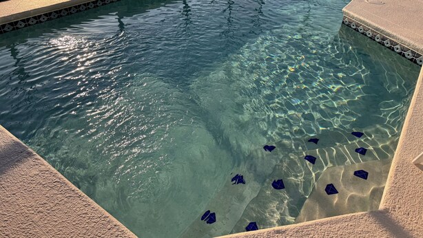 Ein klares Schwimmbecken mit geometrischen Fliesenmustern und einer umgebenden Sonnenterrasse.