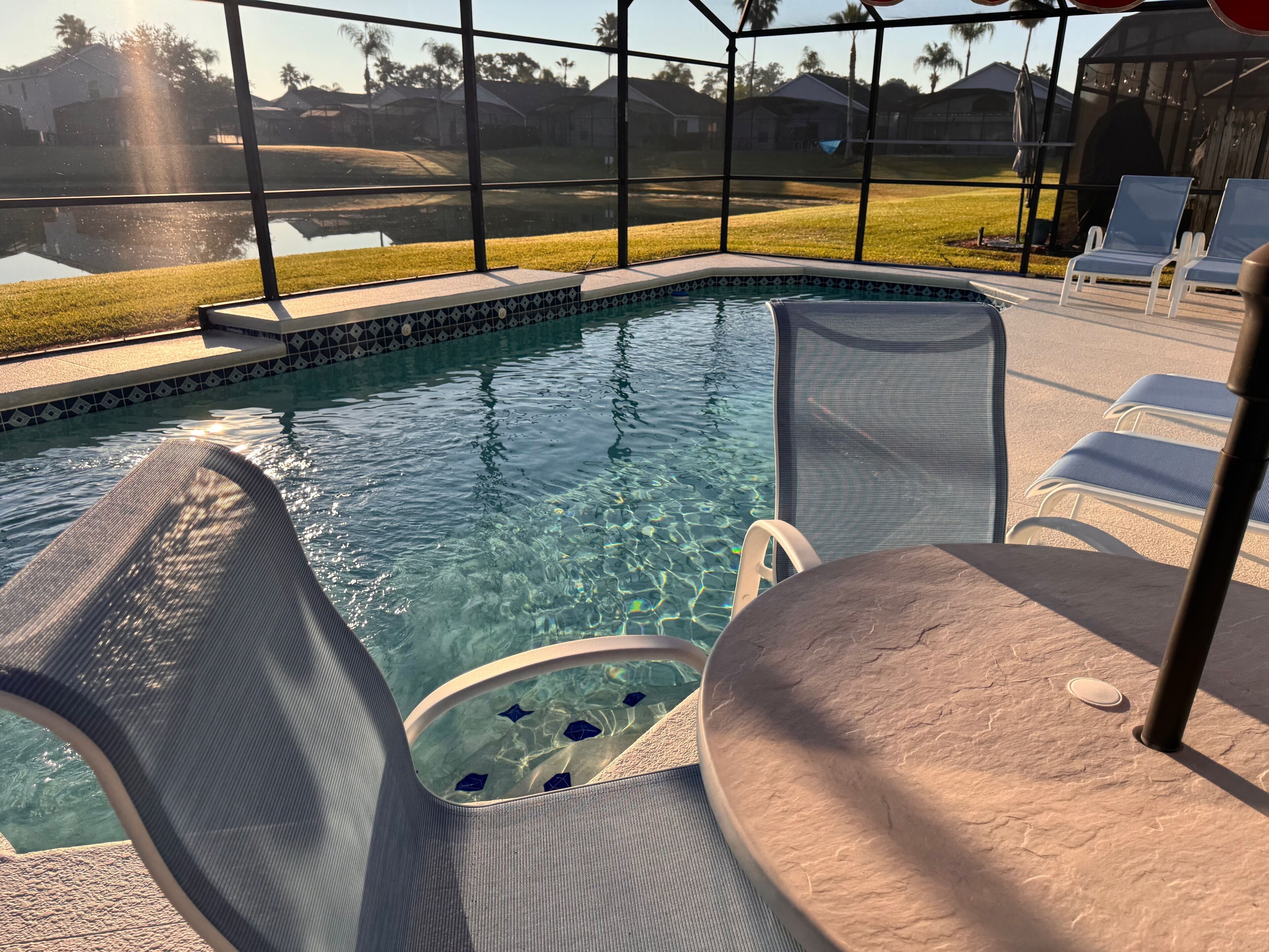 A swimming pool with clear water, surrounded by lounge chairs and a covered patio area.