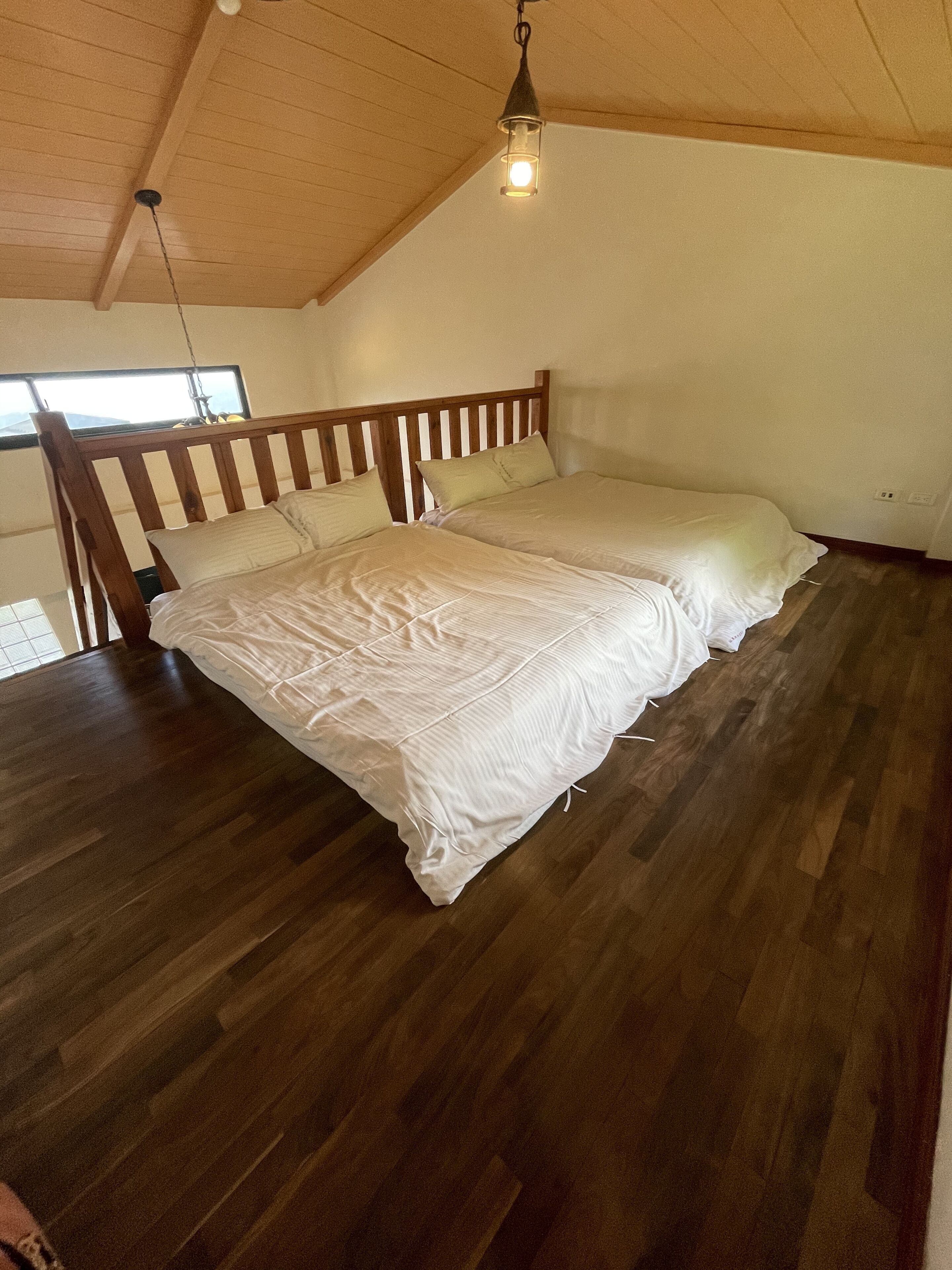 Un dormitorio con estructura de cama de madera, ropa de cama blanca y techo inclinado con una lámpara colgante.