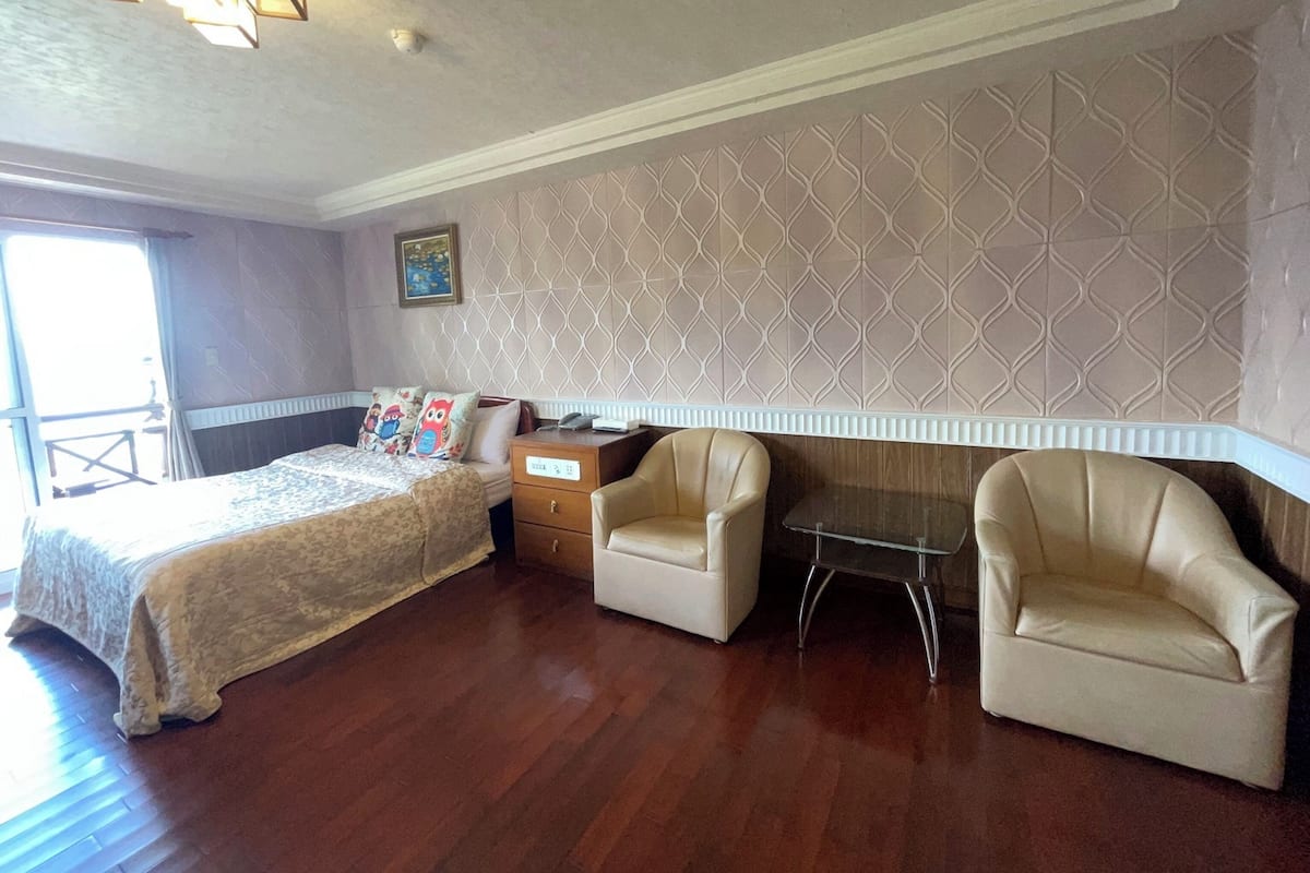 Une chambre d’hôtel avec un lit, deux fauteuils, une petite table et un mur décoré d’un motif.