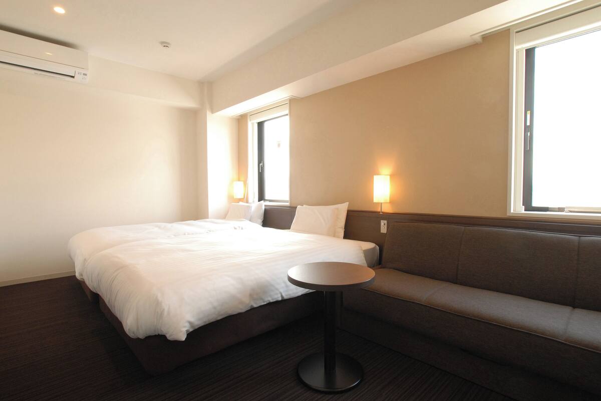 A hotel room with a bed, a round table, a sofa, and two wall-mounted lamps.