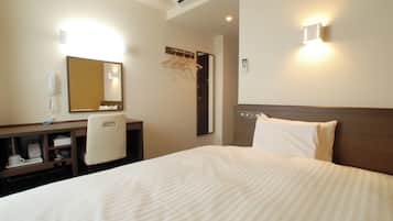 A hotel room with a bed, a desk with a chair, a mirror, a coat rack, and a wall-mounted phone.