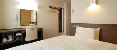 A hotel room with a bed, a desk with a chair, a mirror, a coat rack, and a wall-mounted phone.