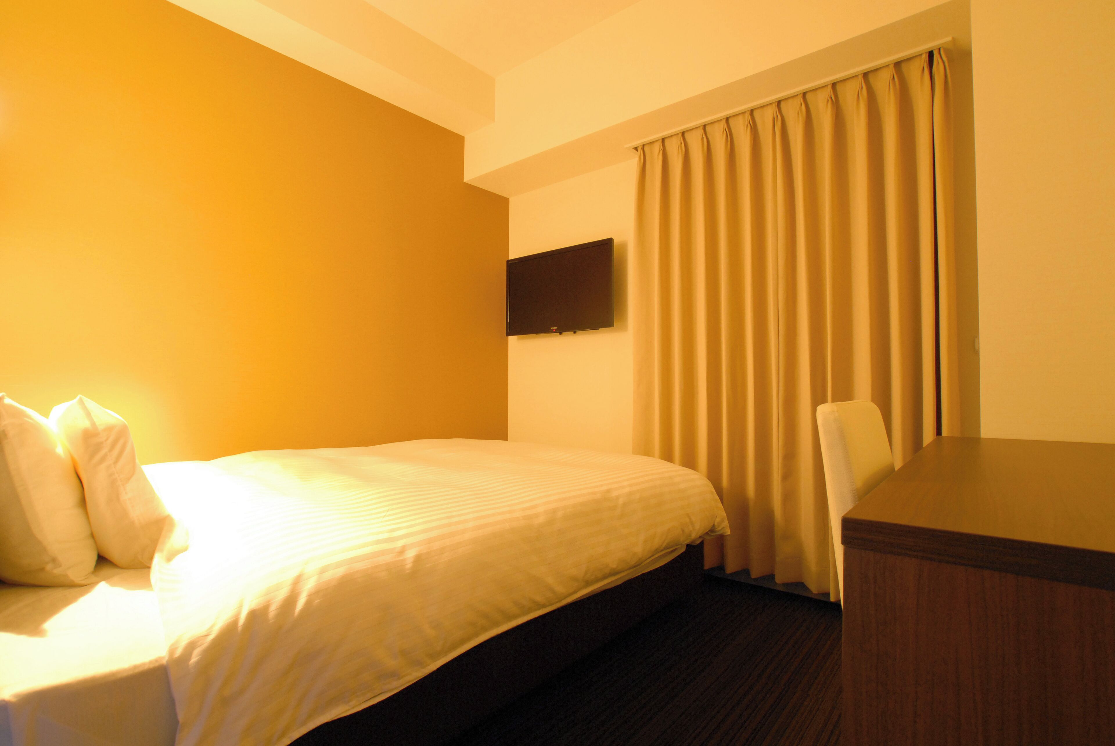A hotel room with a bed, a desk, and a television on the wall.