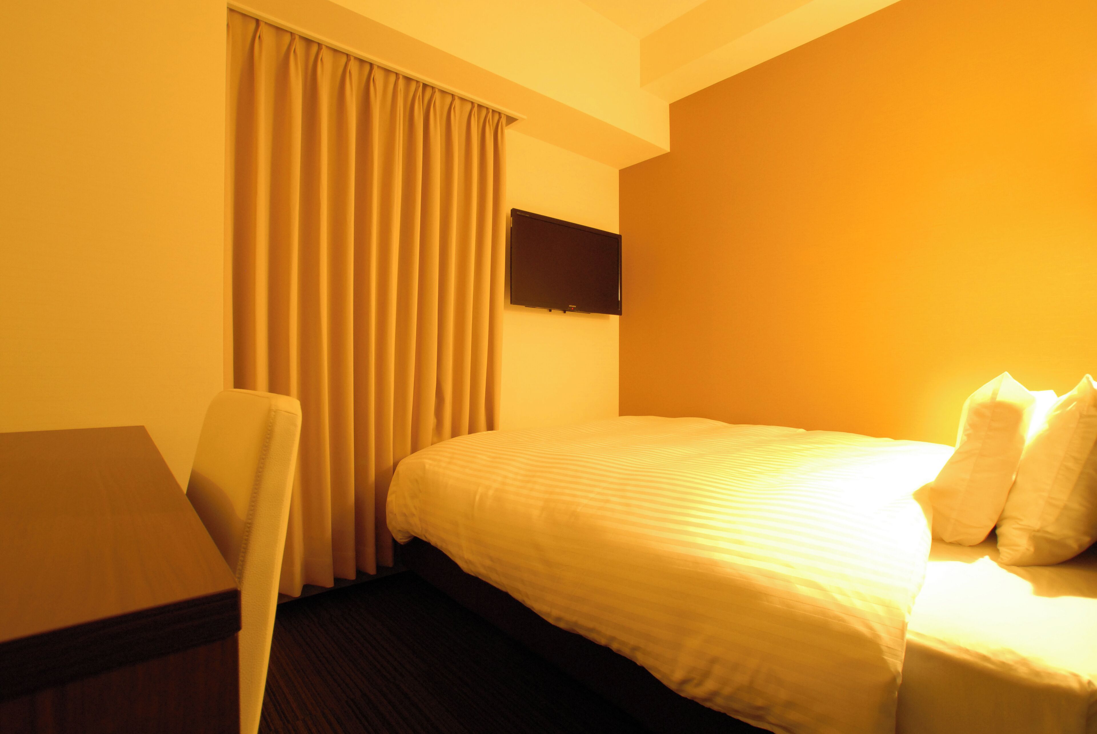 A hotel room with a bed, a chair, a desk, and a flat-screen TV on the wall.