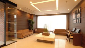 A modern lobby with a large window, a seating area with sofas, a coffee table, and a desk with a laptop. - AB Hotel Fukaya (Fukaya)