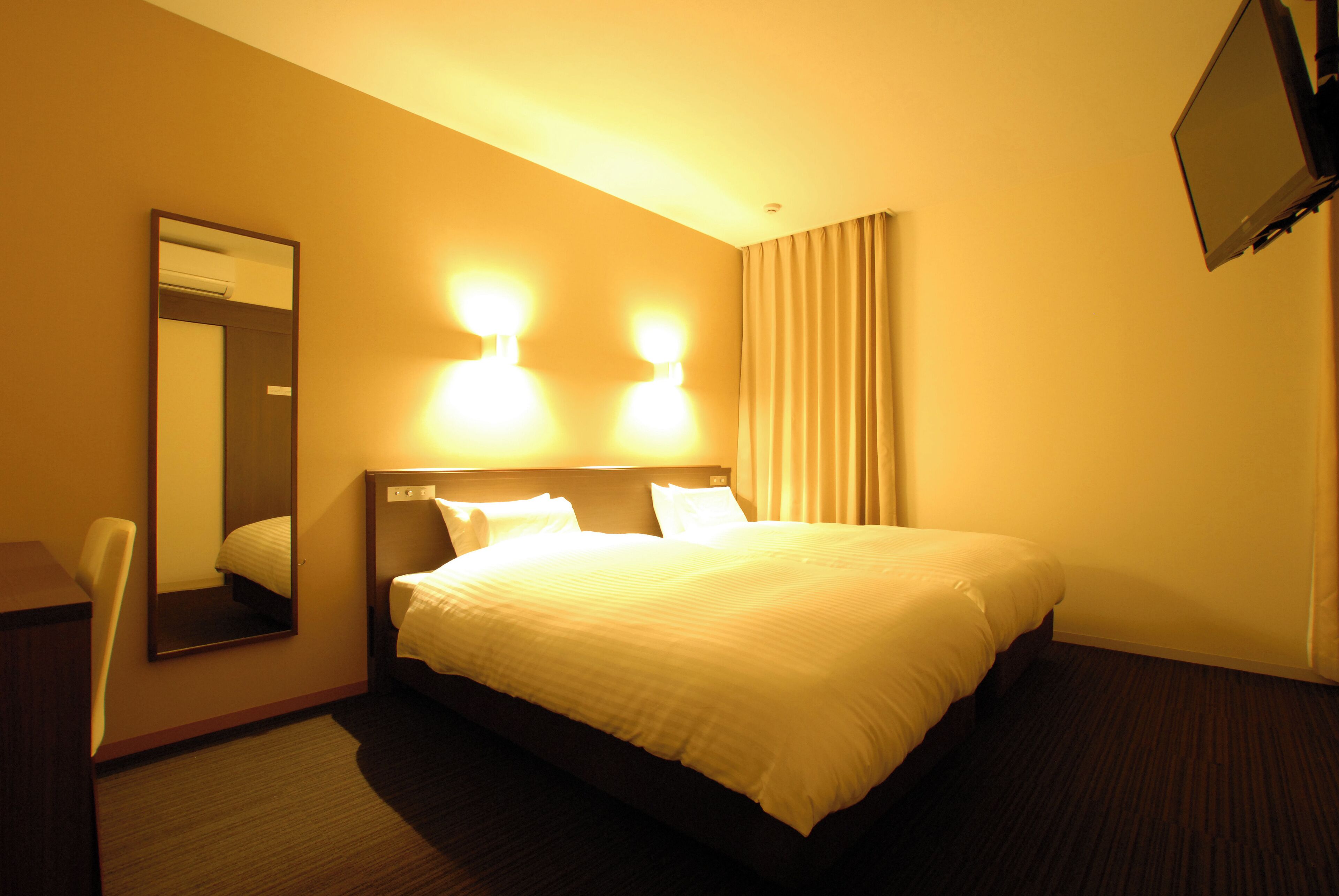 Habitación de hotel con una cama grande, un escritorio, una silla y un televisor de pantalla plana montado en la pared.