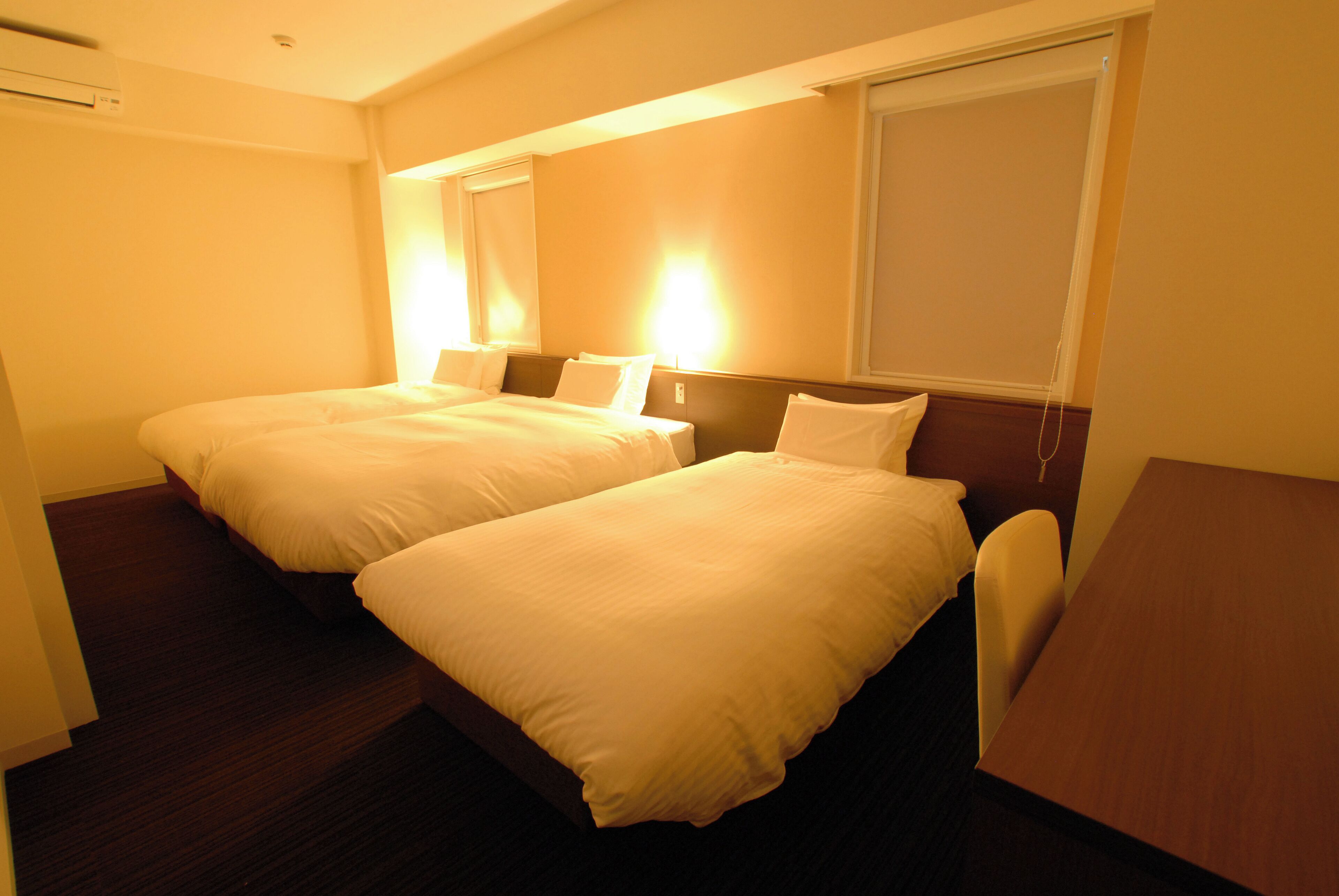 A hotel room with two beds, a wooden headboard, a small table, and a window.