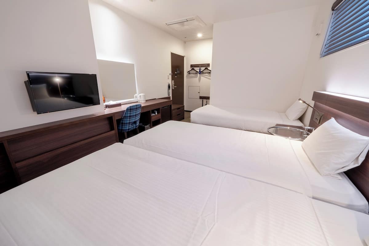 Ein Hotelzimmer mit zwei Betten, einem Fernseher, einem Schreibtisch mit Stuhl, einem Spiegel und einem Kleiderschrank.