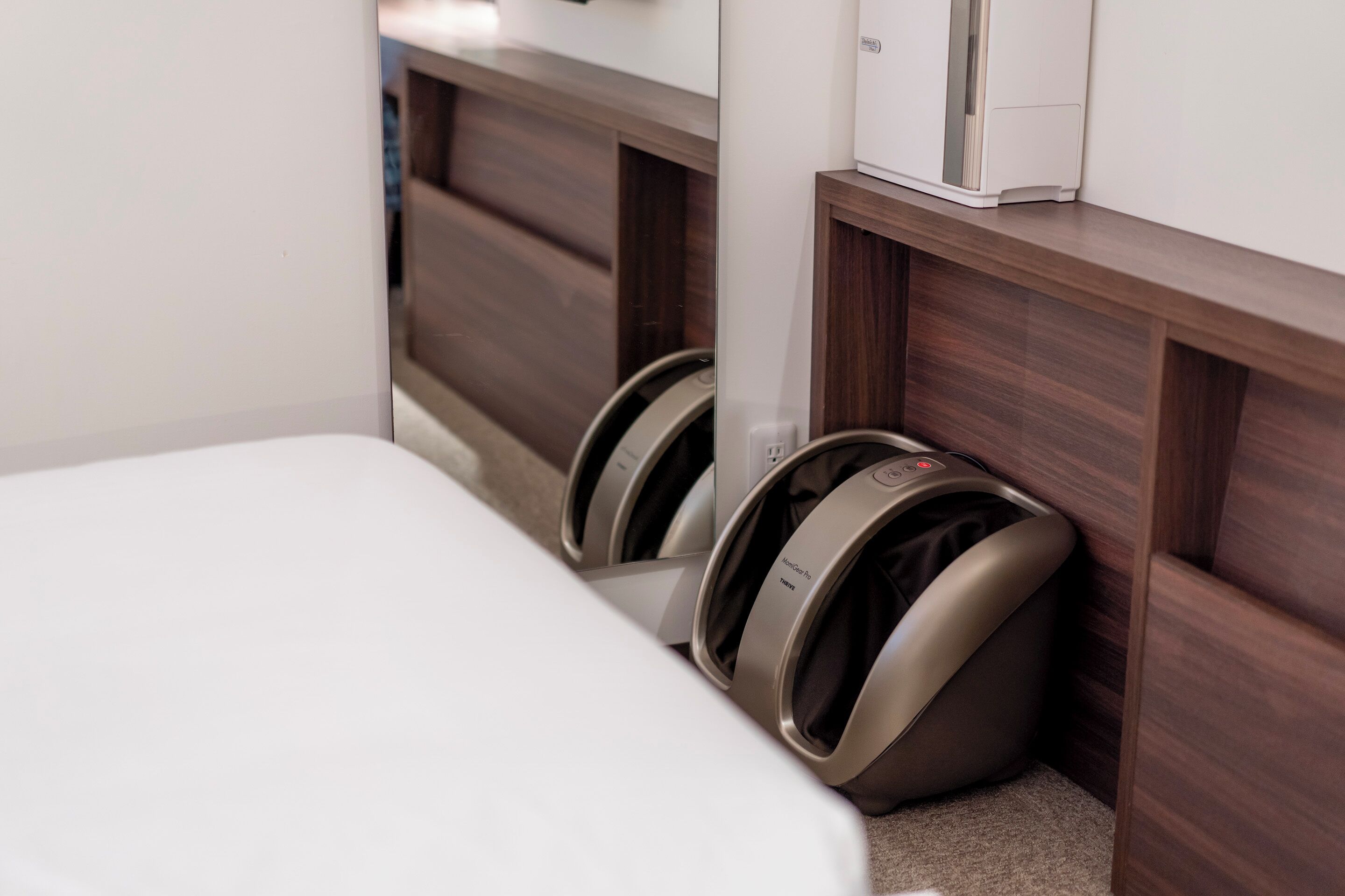 A bed with a headboard, a massage chair, and a white device on a wooden shelf.