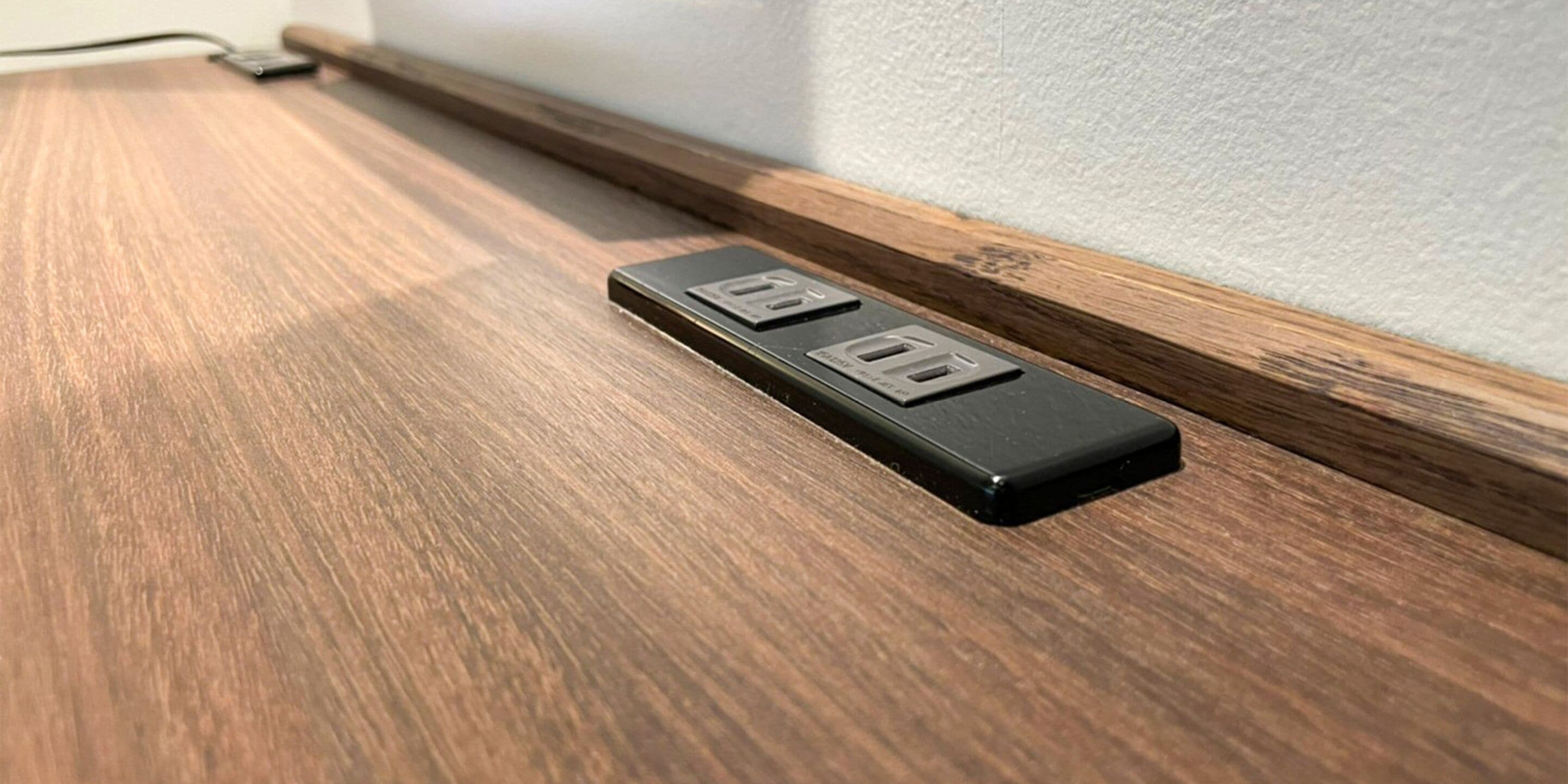 A black power strip with two USB ports and a standard electrical outlet on a wooden surface.