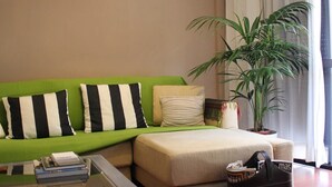 A living room with a green sofa, a beige sofa, a coffee table, a potted plant, and a lamp.