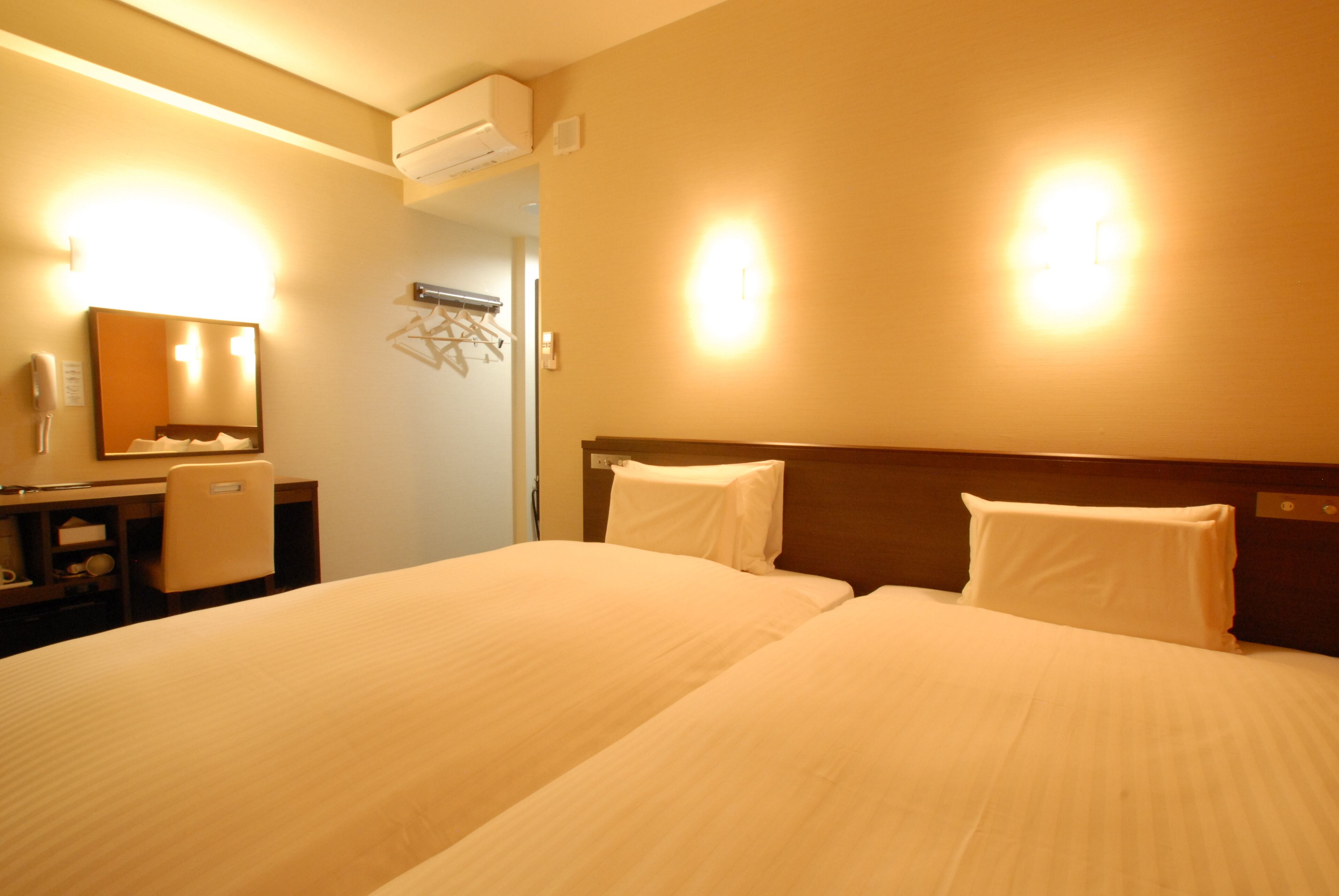 Habitación de hotel con dos camas, un escritorio, un espejo y aire acondicionado instalado en la pared.
