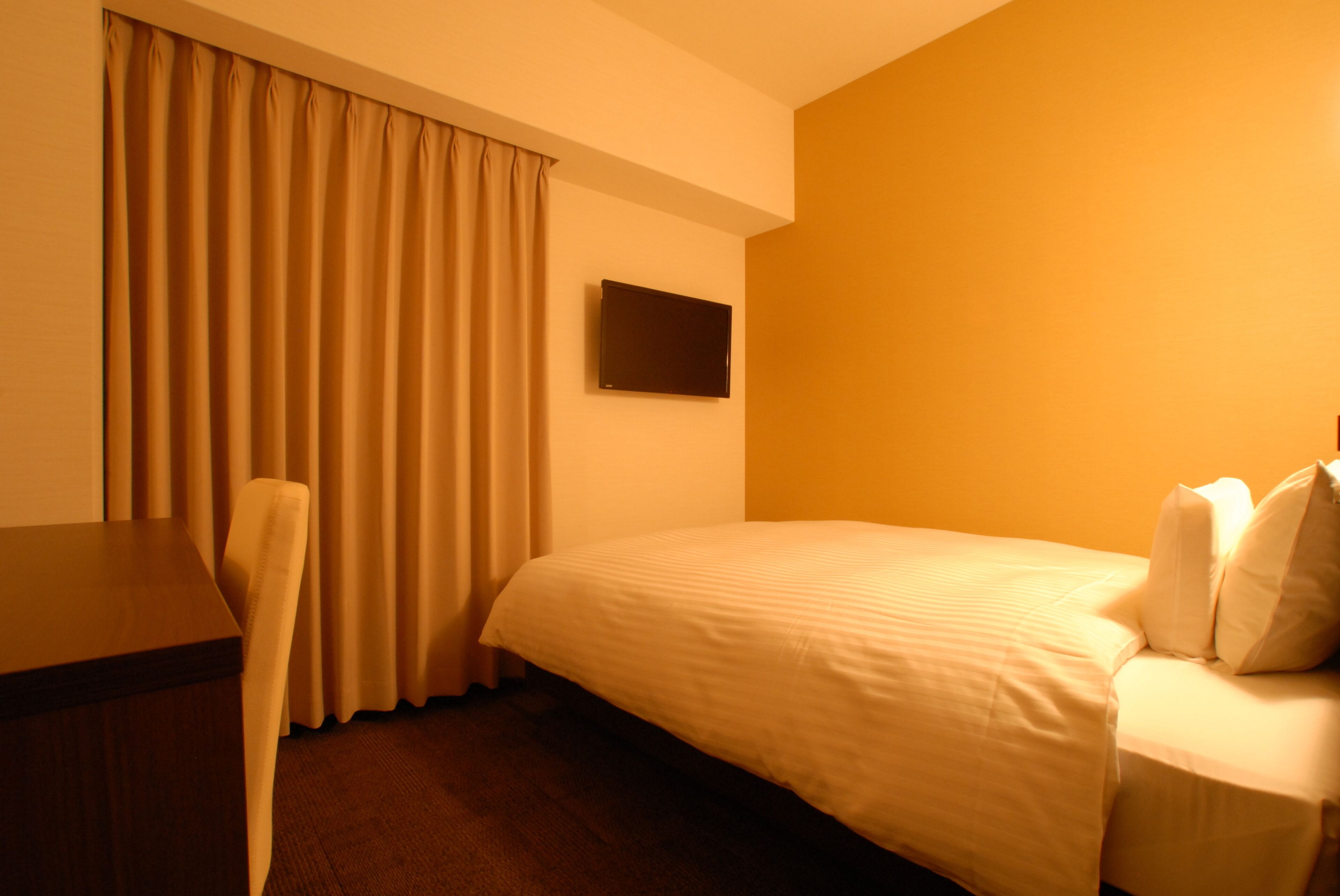 A hotel room with a bed, a desk, a chair, and a TV on the wall.