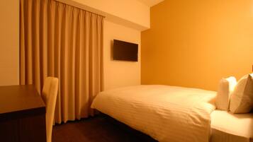 A hotel room with a bed, a desk, a chair, and a TV on the wall.