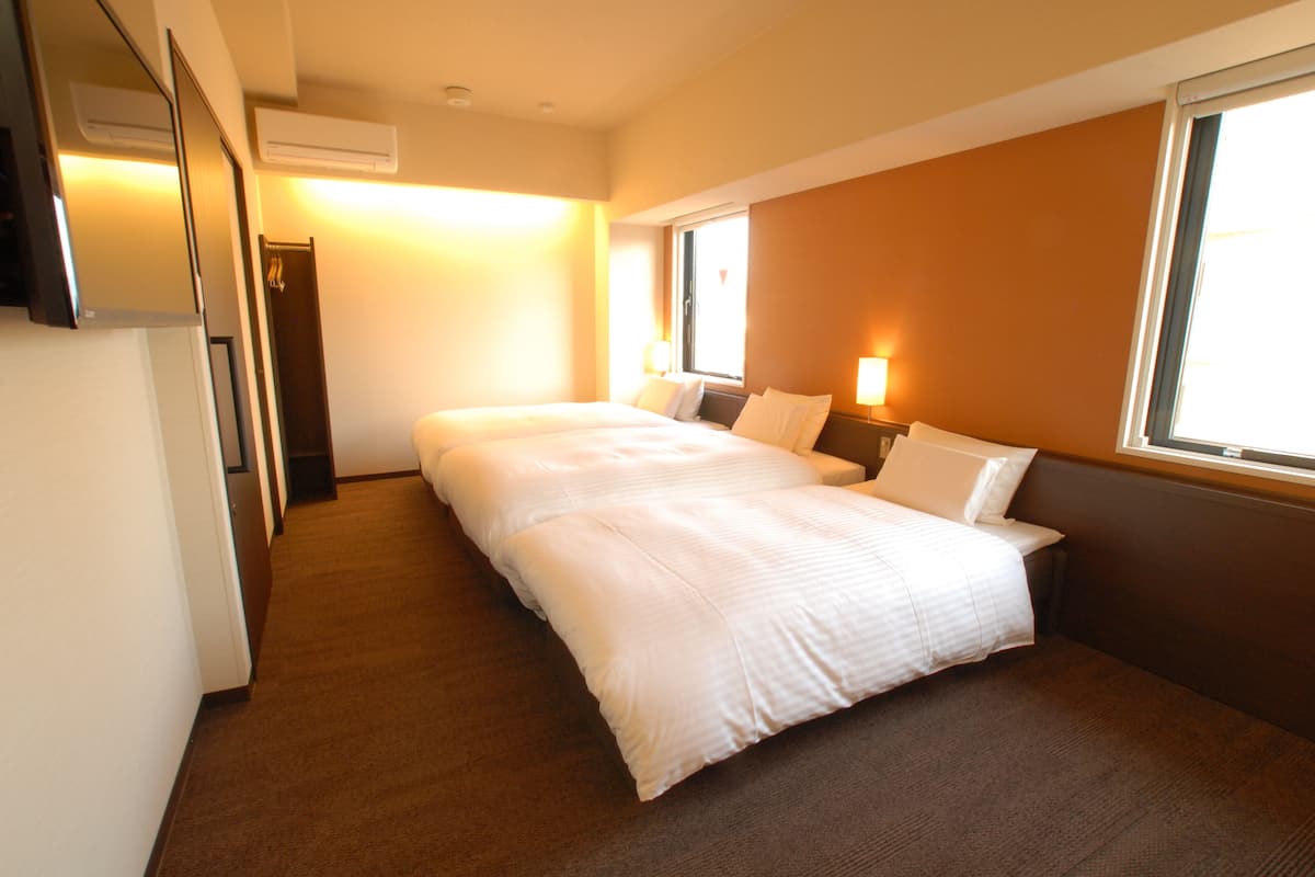 A hotel room with two beds, a window, a wall-mounted TV, and a door.