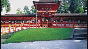 A traditional Japanese building with a red roof and wooden structure, surrounded by a gravel path and green grass.
