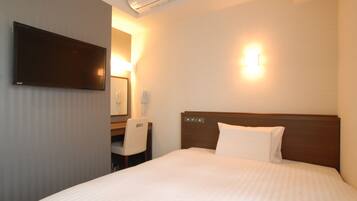 A hotel room with a bed, a desk, a chair, a flat-screen TV, and a wall-mounted light fixture.