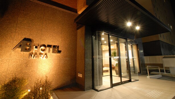 Exterior del ABHOTEL NARA con un diseño moderno, destacando una entrada principal con puertas de cristal y un cartel superior.