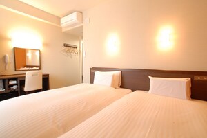 Habitación de hotel con dos camas, un escritorio, una silla, un espejo y aire acondicionado de pared.