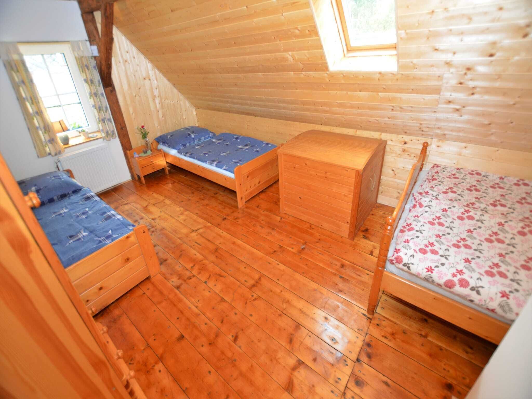 Une petite pièce aux murs lambrissés, comprenant deux lits simples, une commode en bois et une fenêtre laissant entrer la lumière naturelle.
