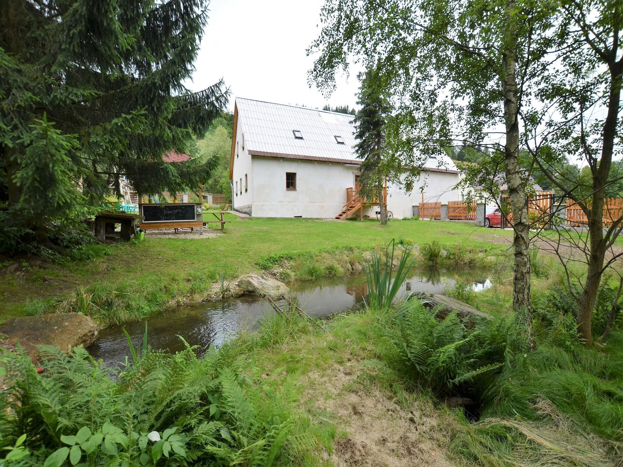 Un bâtiment blanc avec un toit en pente, un petit étang et une végétation luxuriante tout autour.