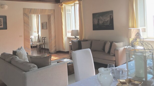 A cozy living room with a sofa, a table with a pitcher, and a lamp. There is a painting on the wall and a window with curtains. - Rome, Historical Center, Via Giulia: unique, elegant, bright, 2 bedrooms, 2 bath (Roma)