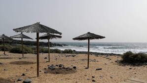 A sandy beach with wooden walkways and thatched umbrellas.