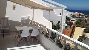 A balcony with a table and chairs, white walls, and a view of the sea.