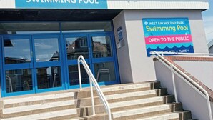 A swimming pool entrance with a blue door and a sign indicating it is open to the public.
