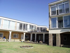 A two-story building with a balcony on the upper floor, a covered patio area, and a small garden in front. - Apartment with stunning Sea View (Bridport)