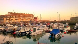 A marina with various boats docked, a building with multiple windows, and a clear sky.