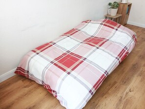A single bed with a plaid bedspread in a room with wooden flooring and a white wall. - Apartment with stunning Sea View (Bridport)