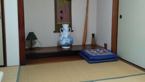 Una habitación tradicional japonesa con suelo de tatami, un panel shoji, un adorno de madera colgante, un jarrón y un tapete azul.