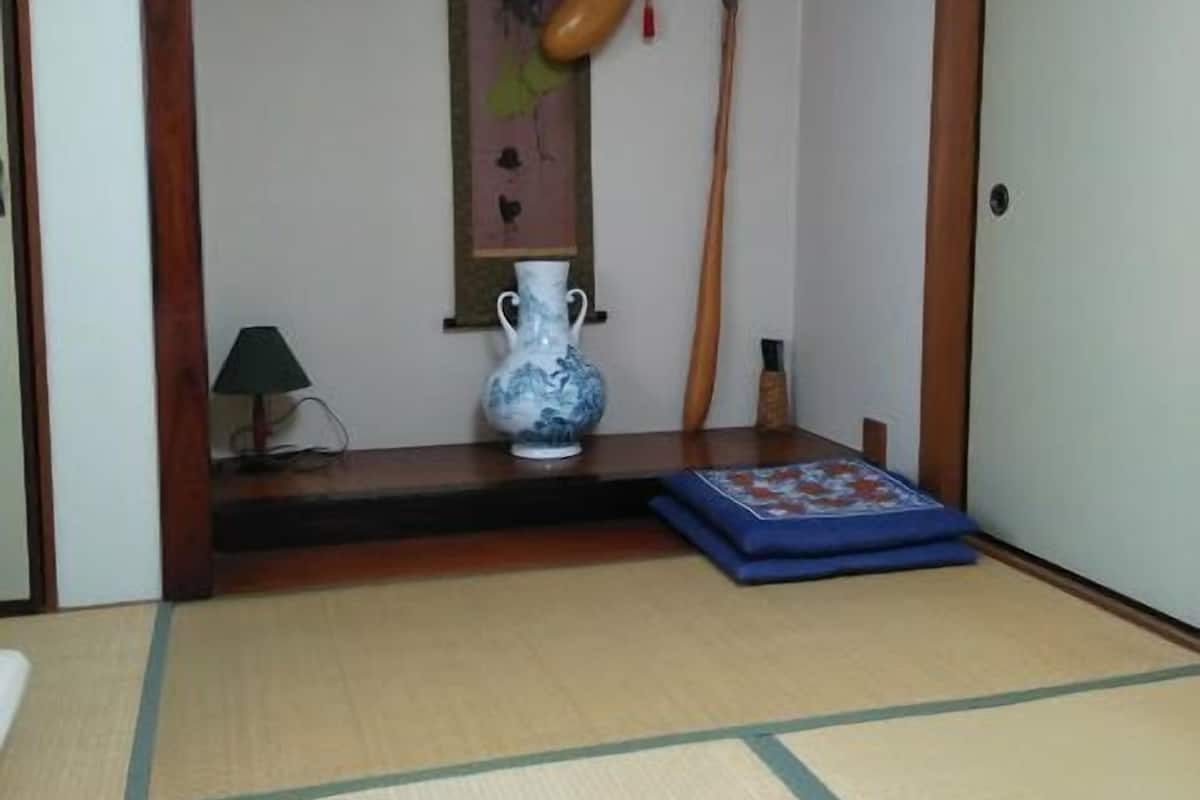 Une pièce de style japonais traditionnel, avec un sol recouvert de tatamis, un paravent shoji, une lanterne suspendue, une flûte en bois et un vase.