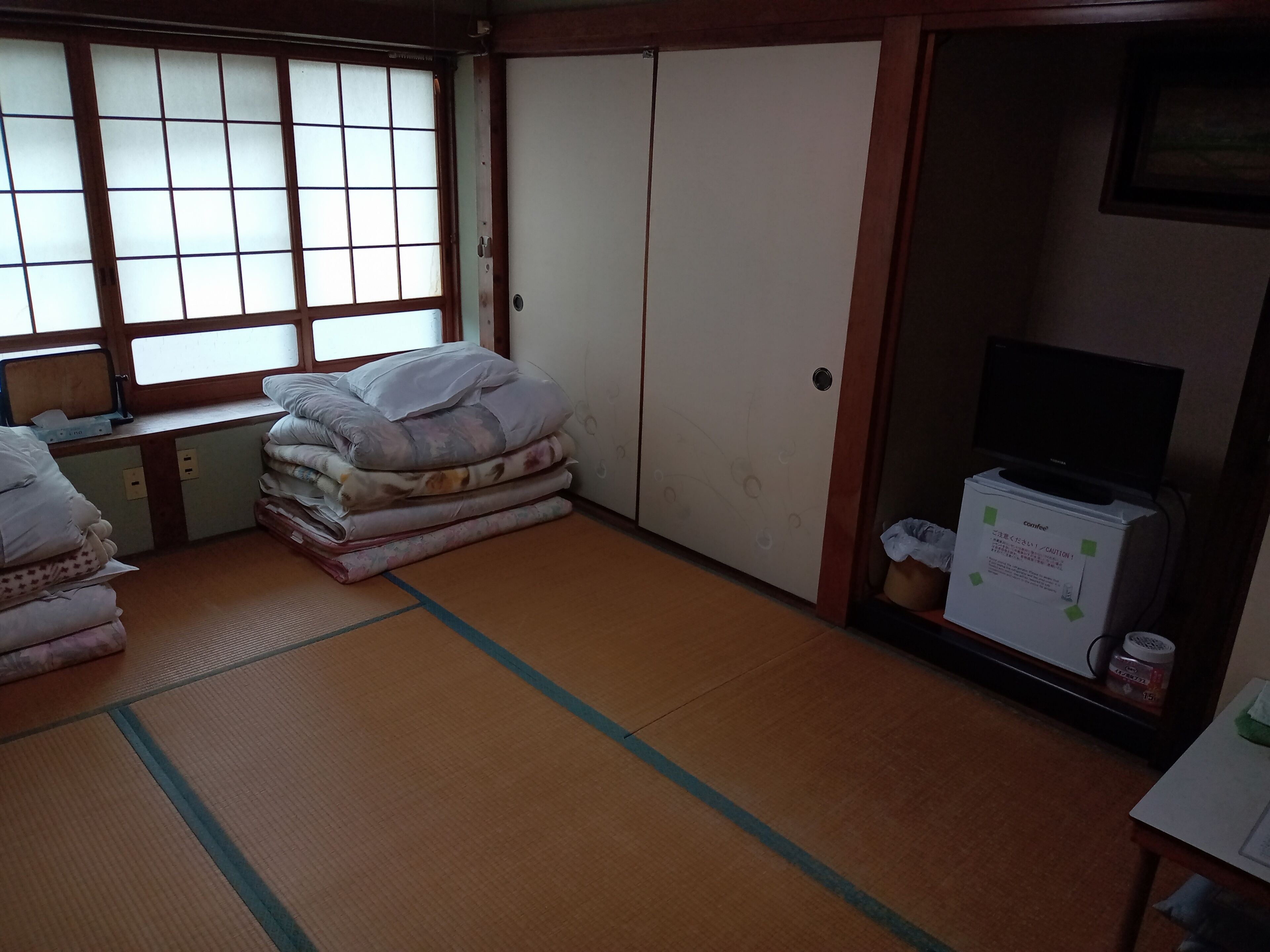 A traditional Japanese room with tatami flooring, a futon bed, a television, and a small cabinet.