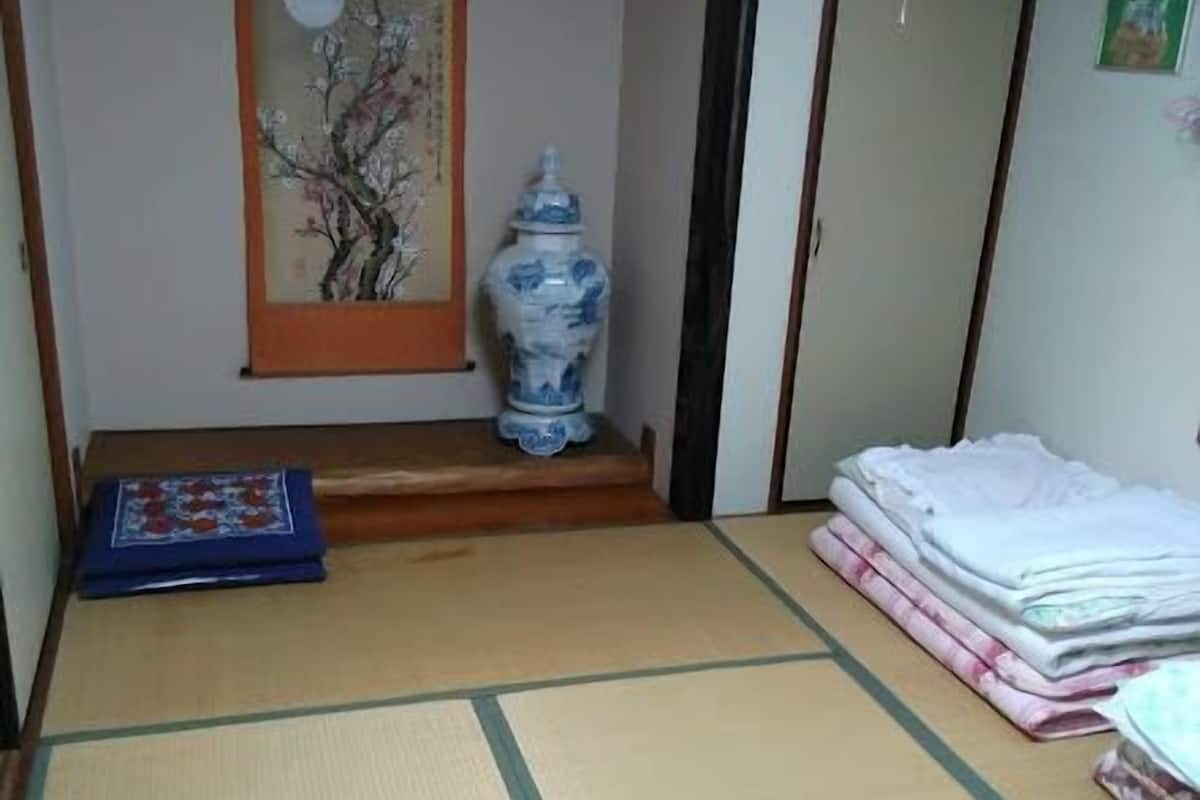Une pièce avec un sol recouvert de tatamis, ornée d’un vase japonais traditionnel, d’un matelas plié et d’une pile de serviettes blanches.