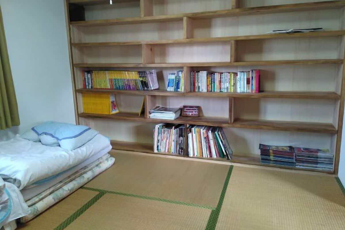 Une pièce avec un lit, un sol recouvert de tatamis et une bibliothèque en bois remplie de livres.