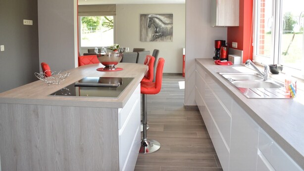 Una cocina moderna con una isla central, sillas rojas y vistas al comedor.