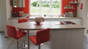 Una cocina moderna con una isla central, sillas rojas y un amplio ventanal con vistas a zonas verdes.